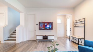 A modern living room with a flat-screen TV mounted on the wall, a staircase, a blue patterned rug, and a blue armchair. - Quiet Charlotte Home, Sleeps 8, Near Uptown (Charlotte)