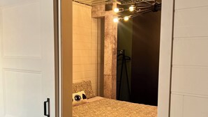 A room with a bed, a door, a concrete pillar, and a ceiling with exposed beams and lighting. - 163 au coeur du centre-ville! (Drummondville)