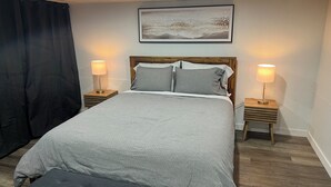 A bedroom with a bed, two bedside tables, a headboard, a wall-mounted painting, and a black curtain. - 163 au coeur du centre-ville! (Drummondville)
