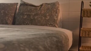 A bed with patterned bedding, a bedside table, and a wall-mounted shelf with baskets. - 163 au coeur du centre-ville! (Drummondville)