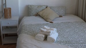 Ein ordentlich bezogenes Bett mit gemusterten Betttextilien, ein Nachttisch mit Lampe und eine gewebte Wanddekoration.