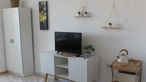 Ein Wohnzimmer mit einer weißen Unterhaltungseinheit, einem Flachbildfernseher, einer Topfpflanze, einem Wasserkocher und einem kleinen Regal mit Dekoration.
