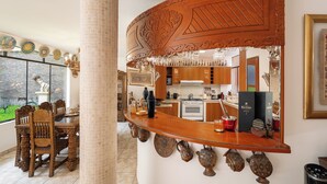 Una zona de bar con una barra de madera curvada, un comedor con mesa y sillas, y una cocina al fondo.