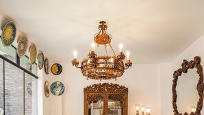 Un comedor con una gran mesa de madera, sillas ornamentadas, un candelabro y placas decorativas en la pared.