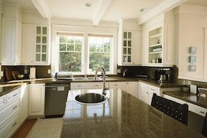 A kitchen with a central island, white cabinetry, and a window providing natural light. - Ocean-View Spa Home / Sauna · Cold Plunge · Hot Tub / Sleeps 10 (Long Beach)