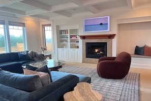 A living room with a fireplace, a sofa, a red chair, and a bookshelf. - Ocean-View Spa Home / Sauna · Cold Plunge · Hot Tub / Sleeps 10 (Long Beach)