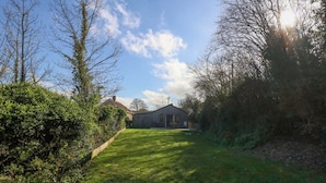 A grassy yard with a building in the distance, surrounded by trees and shrubs. - The Pebble (Dorchester)