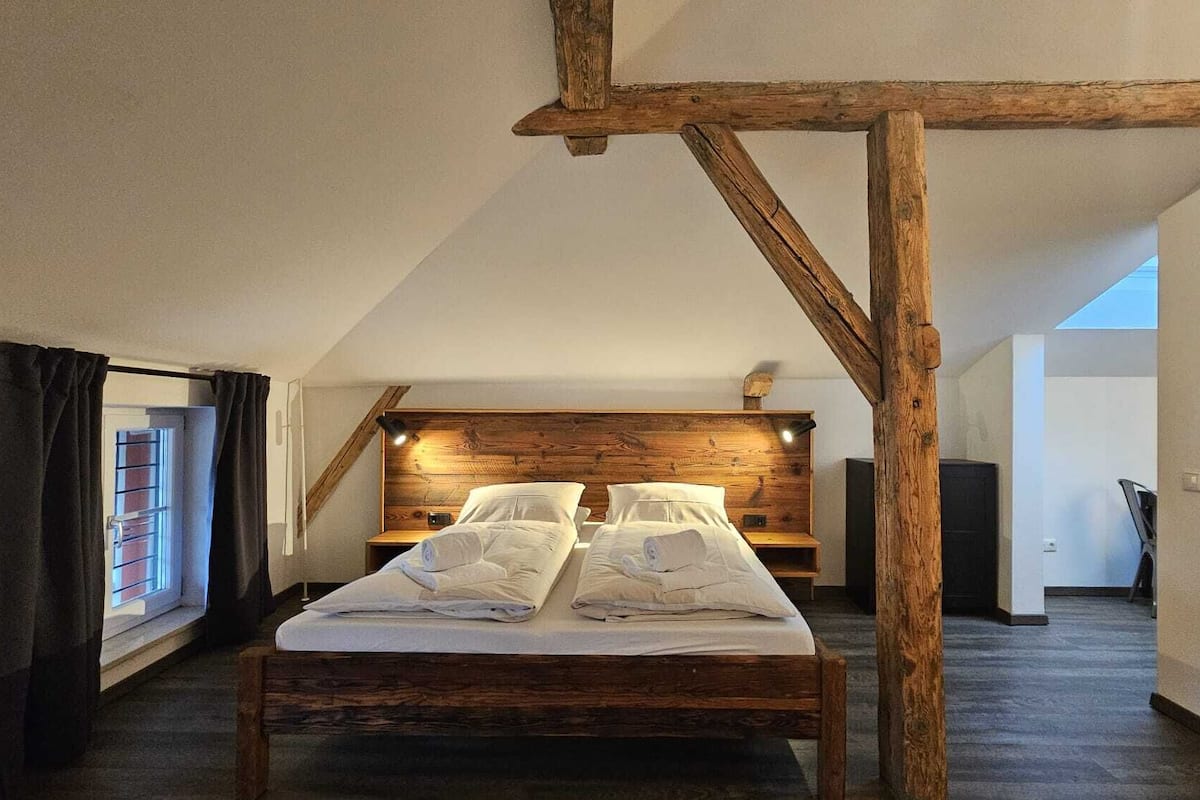 A room with a wooden bed, a sloped ceiling, and a window with curtains.