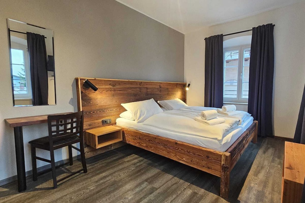 A hotel room with a wooden bed, a desk, a chair, and a window with curtains.