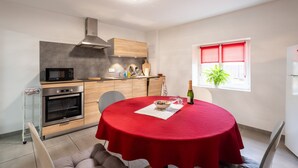 Une cuisine moderne équipée d’un four à micro-ondes, d’un four et de meubles de rangement en bois. On y trouve une table à manger recouverte d’une nappe rouge et une bouteille de vin.