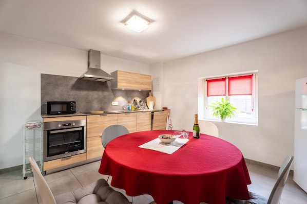 Eine moderne Küche mit Mikrowelle, Backofen und Holzschränken. Ein Esstisch mit roter Tischdecke und einer Weinflasche.