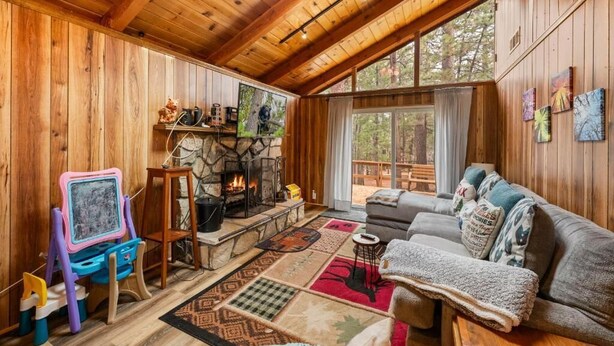 A cozy cabin interior with a stone fireplace, wooden walls, a large window, and a comfortable seating area. - Mama Bear's Cozy Cabin (Sugarloaf)