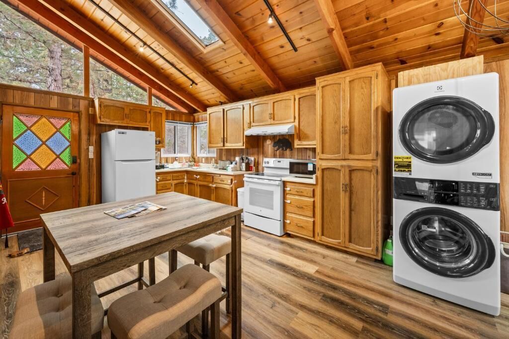 A wooden cabin kitchen with a dining table, wooden cabinets, a washing machine, and a refrigerator.