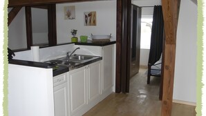 Een kleine keuken met witte kastjes, een spoelbak en een kookplaat. Op het aanrecht staan twee groene vazen.