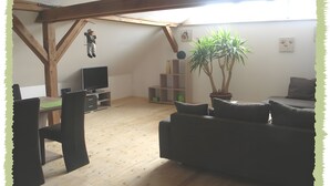 Een woonkamer met een houten plafond, een televisie, een bank en een potplant.