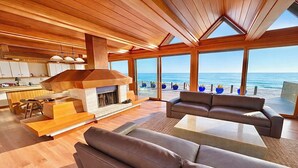 Una sala de estar moderna con chimenea, piso de madera y ventanas amplias con vista al océano.