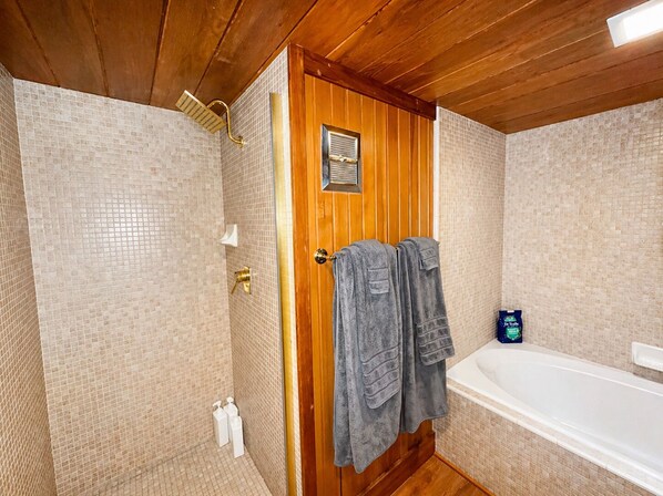 A bathroom with a wooden door, a shower, a bathtub, and a bottle of shampoo.