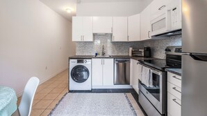 Een kleine keuken met witte kasten, een wasmachine, een vaatwasser, een fornuis en een magnetron.