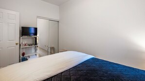 Een slaapkamer met een bed, een televisie op een plank, een kledingkast en een deur.