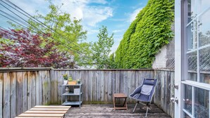 Een houten terras met een stoel en tafels, een houten hek en een groene muur begroeid met klimop.