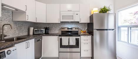 A modern kitchen with stainless steel appliances, white cabinetry, and a large window providing natural light.