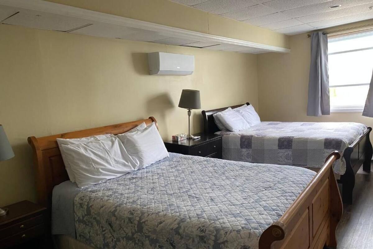 Dos camas con cabeceros de madera, una mesita de noche con lámpara y una ventana con cortinas.