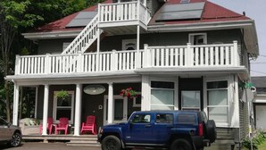 A two-story building with a balcony, a porch with chairs, and a vehicle parked in front. - Colonial Charm Inn  (Charlottetown)