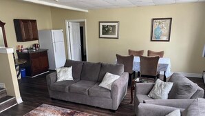 A living room with a gray sofa, a coffee table, and a dining area with chairs and a table. - Colonial Charm Inn  (Charlottetown)
