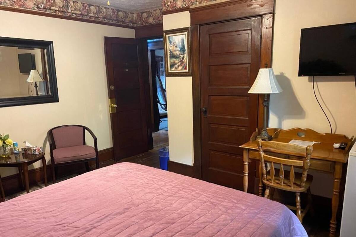 Una habitación de hotel con cama, escritorio, silla, televisor y puerta.