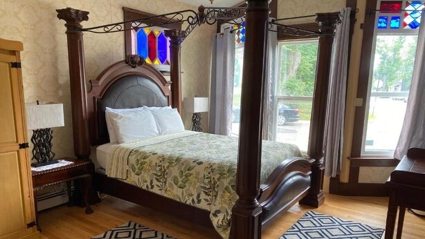 A four-poster bed with a floral bedspread, wooden nightstands, and a patterned rug. - Colonial Charm Inn  (Charlottetown)