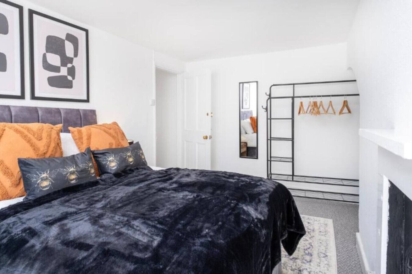 Une chambre à coucher avec un lit, des oreillers, une couvre-lit en velours noir, un mur blanc, un miroir et un porte-manteau avec des vêtements suspendus.