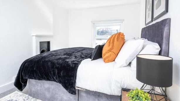 Ein Schlafzimmer mit einem Bett, einer Nachttischlampe, einem Fenster und einer kleinen Pflanze.