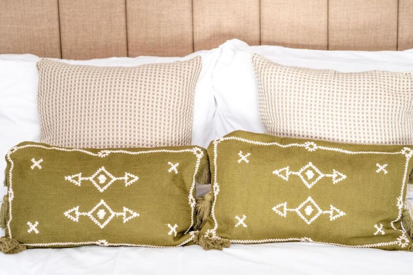 Een bed met wit beddengoed en twee sierkussens met geometrische patronen.