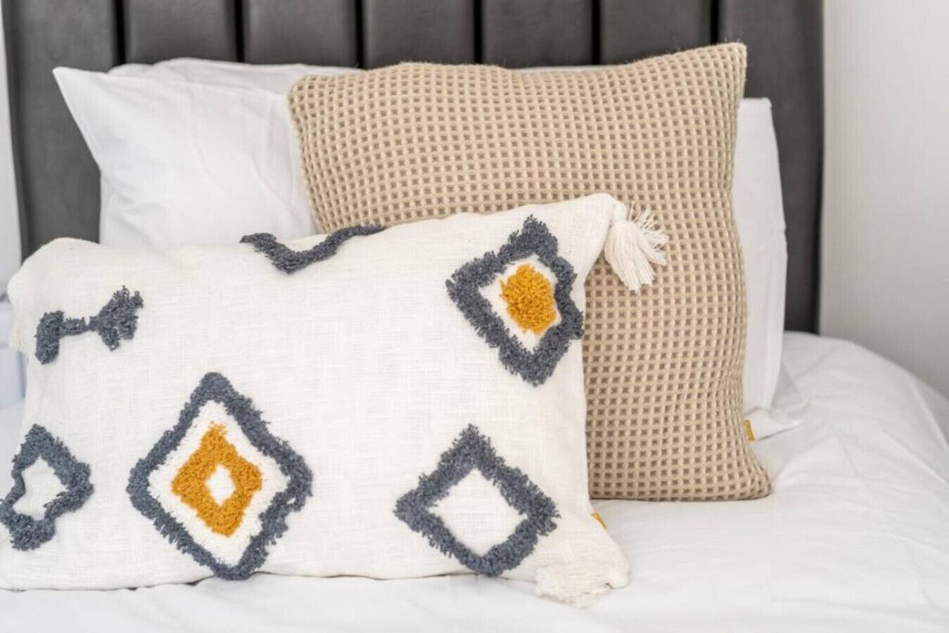 A bed with two pillows, one with a geometric pattern and the other with a textured surface.