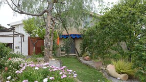 Ein Garten mit blühenden Pflanzen, einem Baum und einem Gebäude mit einer blauen Markise.