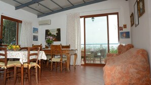 Ein Essbereich mit Tisch und Stühlen, einer Couch, einem Balkon mit Blick und einer Decke mit freiliegenden Balken.