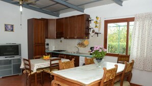 Eine Küche mit Holzschränken, einem Esstisch mit Stühlen, einem Fernseher und einem Fenster mit Vorhängen.