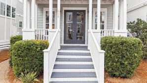 A front entrance with a dark-colored door, white columns, and a white porch railing. - Seacrest Beach House with Pool Access (Inlet Beach)