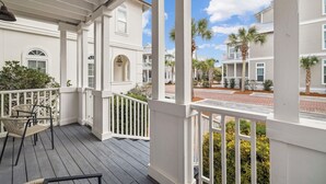 A covered porch with a railing, wicker chairs, and a view of neighboring houses. - Seacrest Beach House with Pool Access (Inlet Beach)