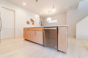 A modern kitchen with wooden cabinets, stainless steel appliances, pendant lighting, and a window.