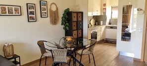 A dining area with a glass table and wicker chairs, a kitchen with modern appliances, and a living area with a sofa and wall art. - Charming and cosy apartment with terrace and pool view, 2 steps from the Marina (Albufeira)