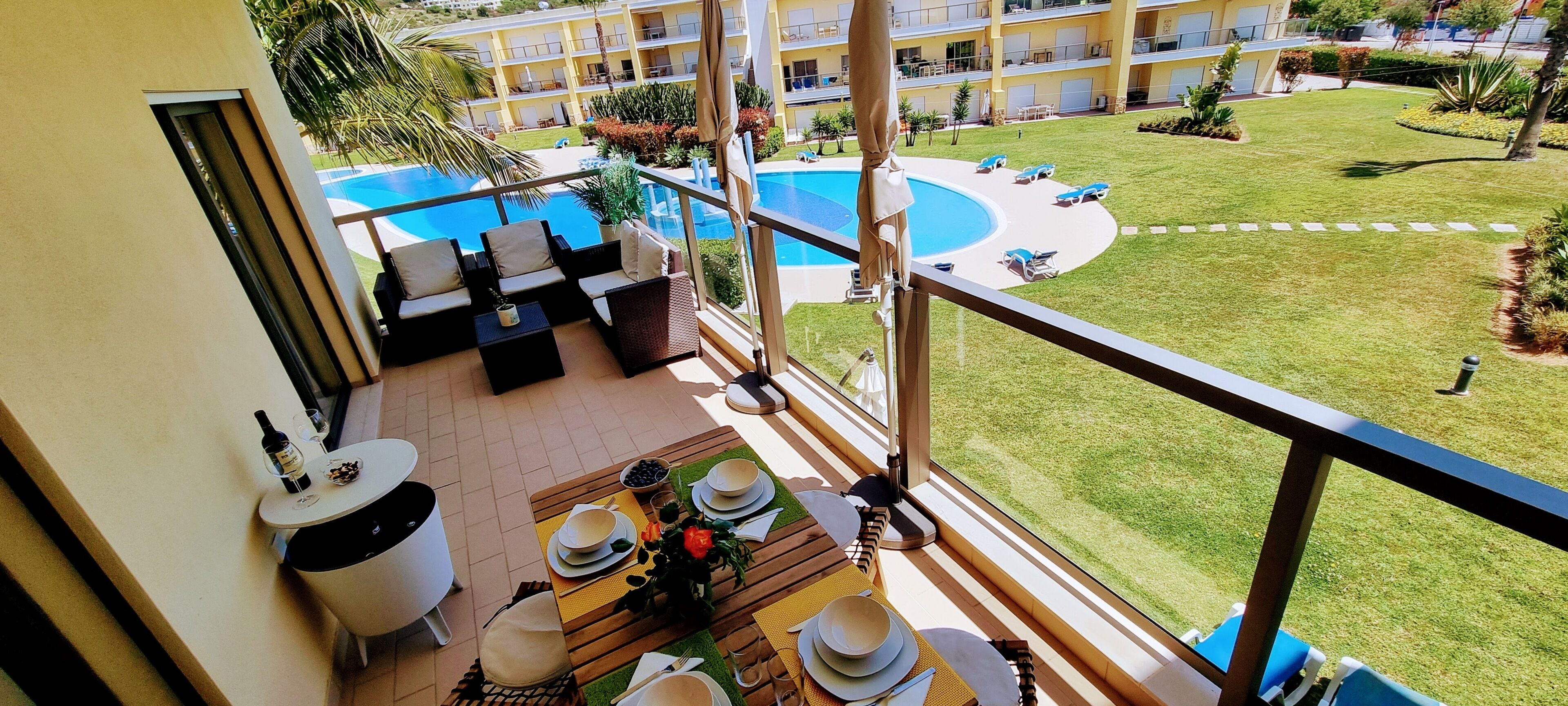 Un balcone con vista sulla piscina, arredi da esterno e zona pranzo con tavola apparecchiata.