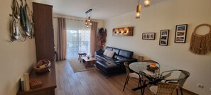 A living room with a black leather sofa, a glass coffee table, and a dining table with chairs. There is a decorative wall hanging and a framed picture on the wall. - Charming and cosy apartment with terrace and pool view, 2 steps from the Marina (Albufeira)