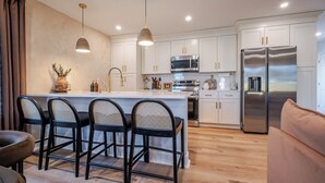 A modern kitchen with white cabinets, a stainless steel refrigerator, and a central island with bar stools. - Renovated Spacious Home Near Downtown, Sleeps 10 (Richmond)