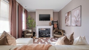 A living room with a fireplace, two armchairs, a sofa, and a TV mounted above the fireplace. - Renovated Spacious Home Near Downtown, Sleeps 10 (Richmond)