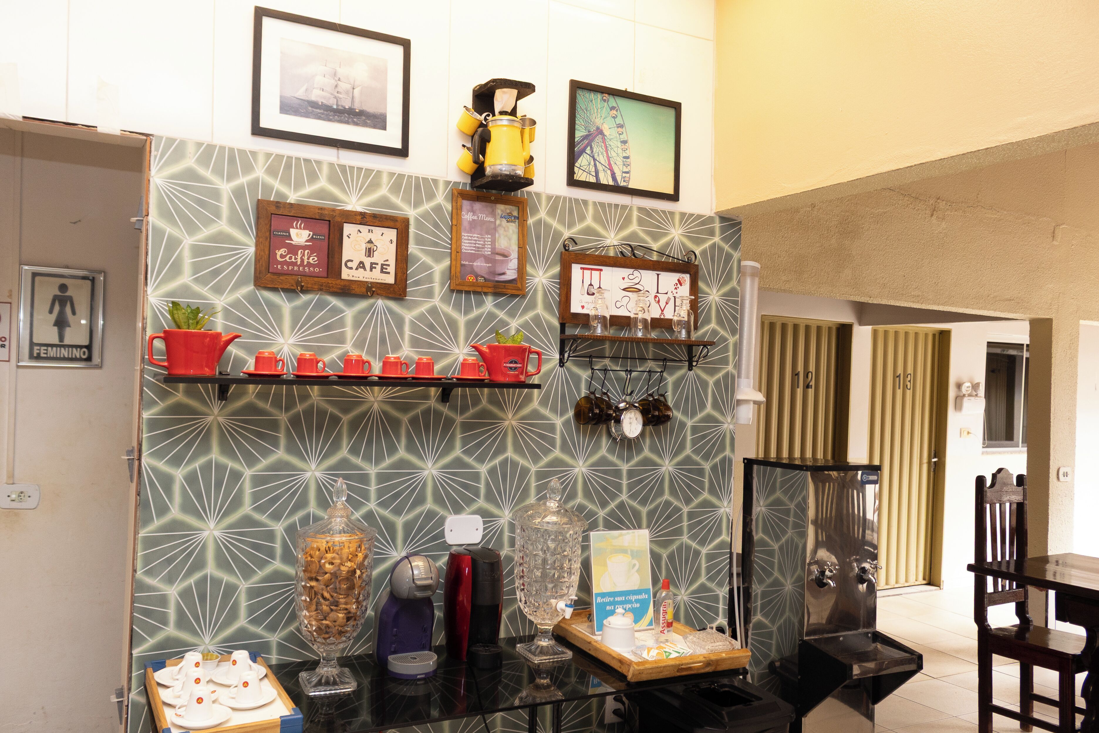 Un vestíbulo de hotel con una estación de café, cuadros enmarcados y un letrero visible del baño.