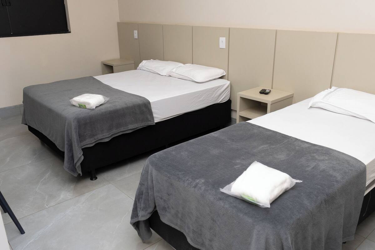 Two single beds with grey bedding, a small bedside table with a phone, and a wall-mounted light switch.