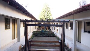 Un patio con una pérgola de madera, un banco y un jardín con flores rojas.