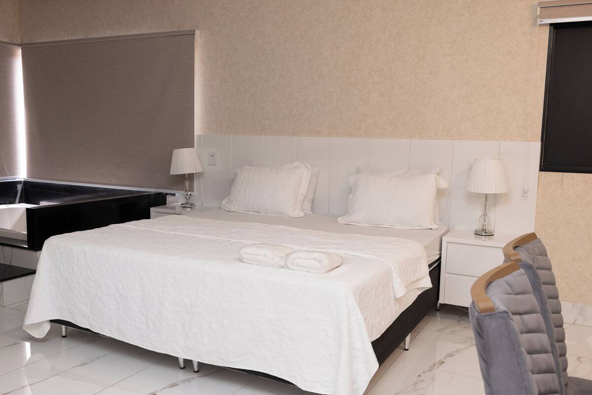 A modern hotel room with a large bed, a bedside table, a nightstand, and a chair.