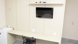 Una habitación con escritorio, silla, televisor y un electrodoméstico blanco pequeño.